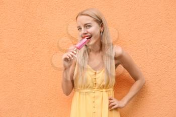 Beautiful young woman with ice cream near color wall�