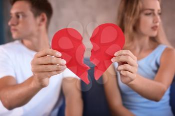 Young couple holding halves of broken heart on sofa at home. Relationship problems�