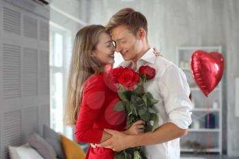 Happy young couple with red roses hugging at home�