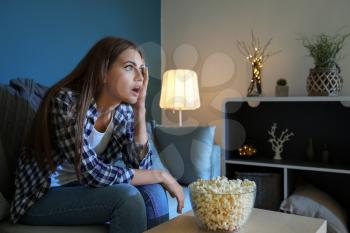 Emotional young woman eating popcorn while watching TV late in evening�