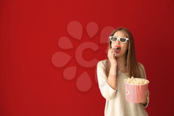 Beautiful young woman with cup of popcorn and 3D cinema glasses on color background�