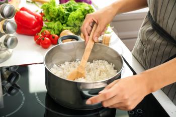 Woman cooking rice in saucepan on stove�