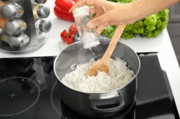 Woman salting boiled rice in kitchen�
