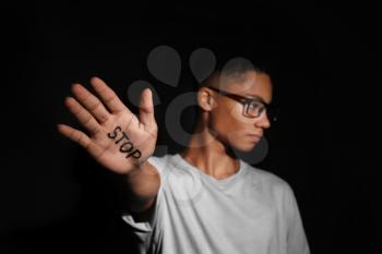 African-American teenage boy with word STOP written on hand against dark background�