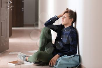 Sad teenage boy sitting on floor indoors. Bullying at school�