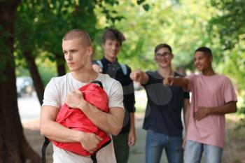 Bullied teenage boy with aggressive schoolmates outdoors�