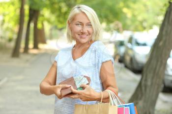 Mature woman with money and shopping bags outdoors�