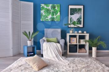 Stylish room interior with armchair and green tropical leaves�