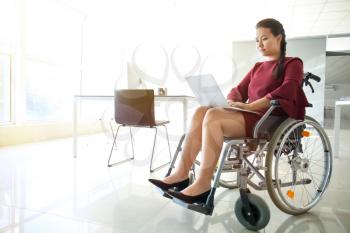 Asian woman in wheelchair working with laptop in office�