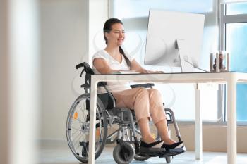 Asian woman in wheelchair working with computer in office�