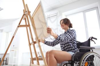 Young female artist in wheelchair painting picture at home�