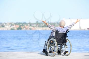 Happy senior woman in wheelchair near river�