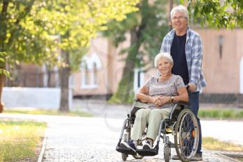 Senior woman in wheelchair and her husband outdoors�