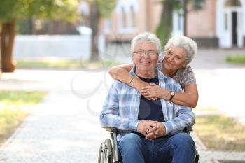 Happy senior man in wheelchair and his wife outdoors�