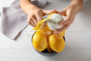 Woman peeling ripe lemons at white wooden table, closeup�