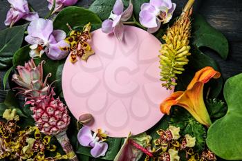 Composition with fresh tropical leaves, flowers and blank card on wooden background�