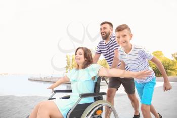 Young woman in wheelchair with her family walking outdoors�