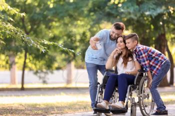 Young woman in wheelchair with her family taking selfie outdoors�