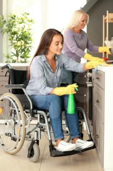 Young woman in wheelchair and her mother cleaning kitchen�