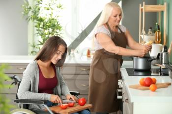 Young woman in wheelchair cooking together with her mother�