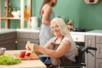 Mature woman in wheelchair cooking together with daughter at home�