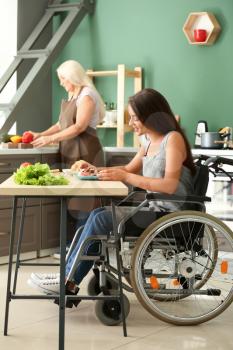 Young woman in wheelchair eating at home�