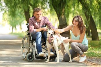 Young man in wheelchair with his wife and service dog outdoors�