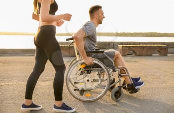 Young man in wheelchair and sporty woman training outdoors�