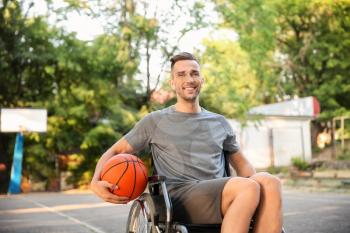 Sporty young man with ball sitting in wheelchair outdoors�