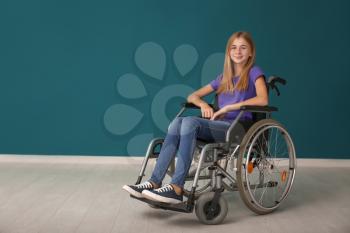 Teenage girl in wheelchair against color wall�