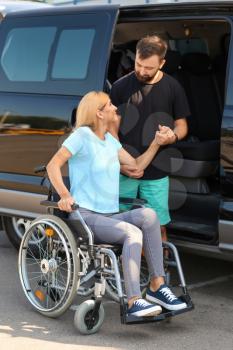 Man helping woman in wheelchair to sit in car�