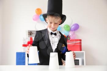 Cute little magician showing tricks with cups indoors�
