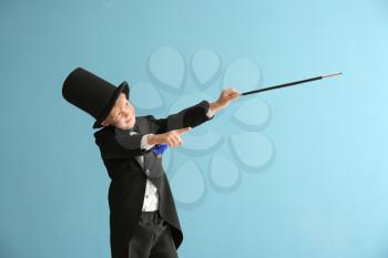 Cute little magician showing trick on color background�