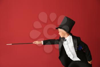 Cute little magician showing tricks on color background�