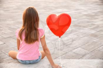 Cute little girl with heart-shaped air balloon sitting on stairs outdoors�