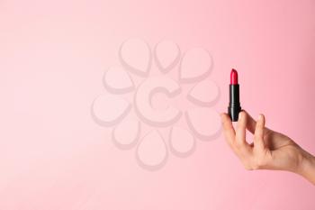 Woman holding bright lipstick on color background�