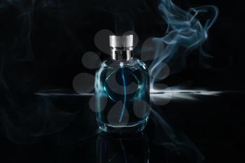 Bottle of perfume with fume on dark background�