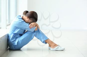 Tired female nurse sitting on floor in hospital�