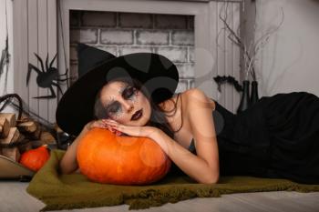 Beautiful woman dressed as witch in room decorated for Halloween�