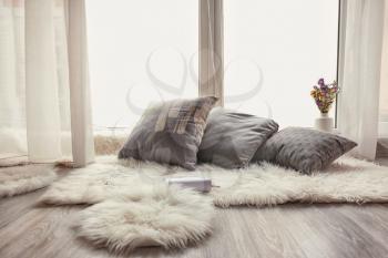 Cozy place for rest with soft pillows and furry rugs near window�