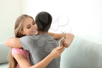 Young woman texting lover while hugging her boyfriend at home�