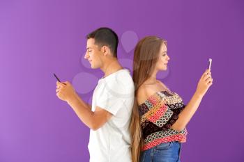 Young couple with mobile phones on color background�
