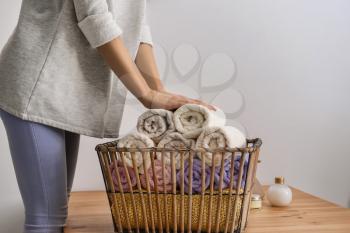 Woman folding clean soft towels into basket at wooden table�