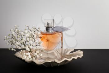 Transparent bottle of perfume with beautiful flowers on dark table�