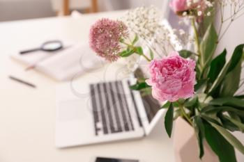 Vase with beautiful pink flowers and laptop on table�