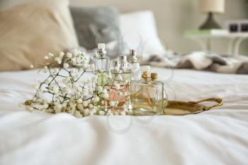 Metal tray with bottles of perfume and flowers on bed�
