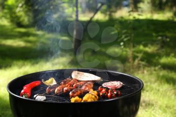 Cooking of tasty sausages and vegetables on barbecue grill outdoors�