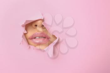 Lips of beautiful young woman visible through hole in pink teared paper�