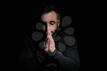 Religious young man praying to God on black background�