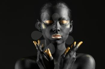 Beautiful woman with black and golden paint on her body against dark background�
